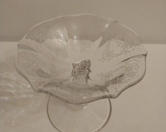 May include: A clear glass pedestal bowl with a scalloped edge and a floral etched design. The bowl is on a clear glass pedestal.