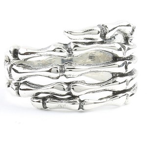 May include: A silver ring shaped like a skeletal hand with the fingers curled inwards. The ring is made of metal and has a detailed design.