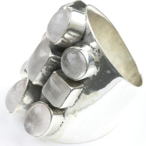 May include: A chunky silver ring featuring multiple light pink gemstones in various shapes. The ring has a wide band and the gemstones are set in individual silver bezels, creating a cluster design. The gemstones have a soft, translucent appearance.