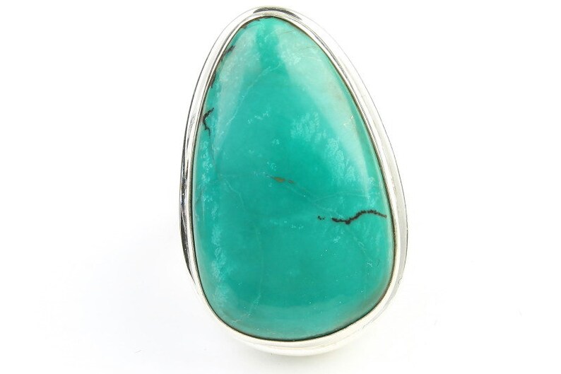 May include: A turquoise ring with a silver setting. The turquoise is a teardrop shape and has a smooth, polished finish.