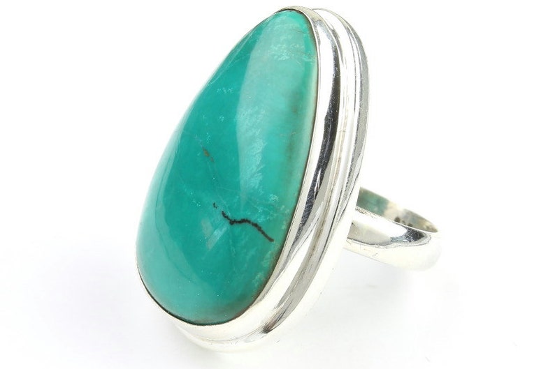 May include: A turquoise ring with a silver band. The turquoise stone is teardrop shaped and has a dark vein running through it.