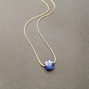 Peut inclure: Un collier délicat en chaîne dorée avec un pendentif en pierre précieuse bleu foncé facetté.