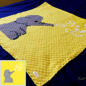 May include: A yellow crocheted baby blanket featuring a grey elephant blowing bubbles. The blanket has a small tag that reads "My Design".