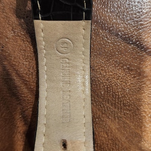 Puede incluir: Primer plano de una correa de reloj de cuero marr&oacute;n con costuras blancas. La correa tiene un forro de cuero blanco con el texto "Genuine Leather" impreso en &eacute;l.