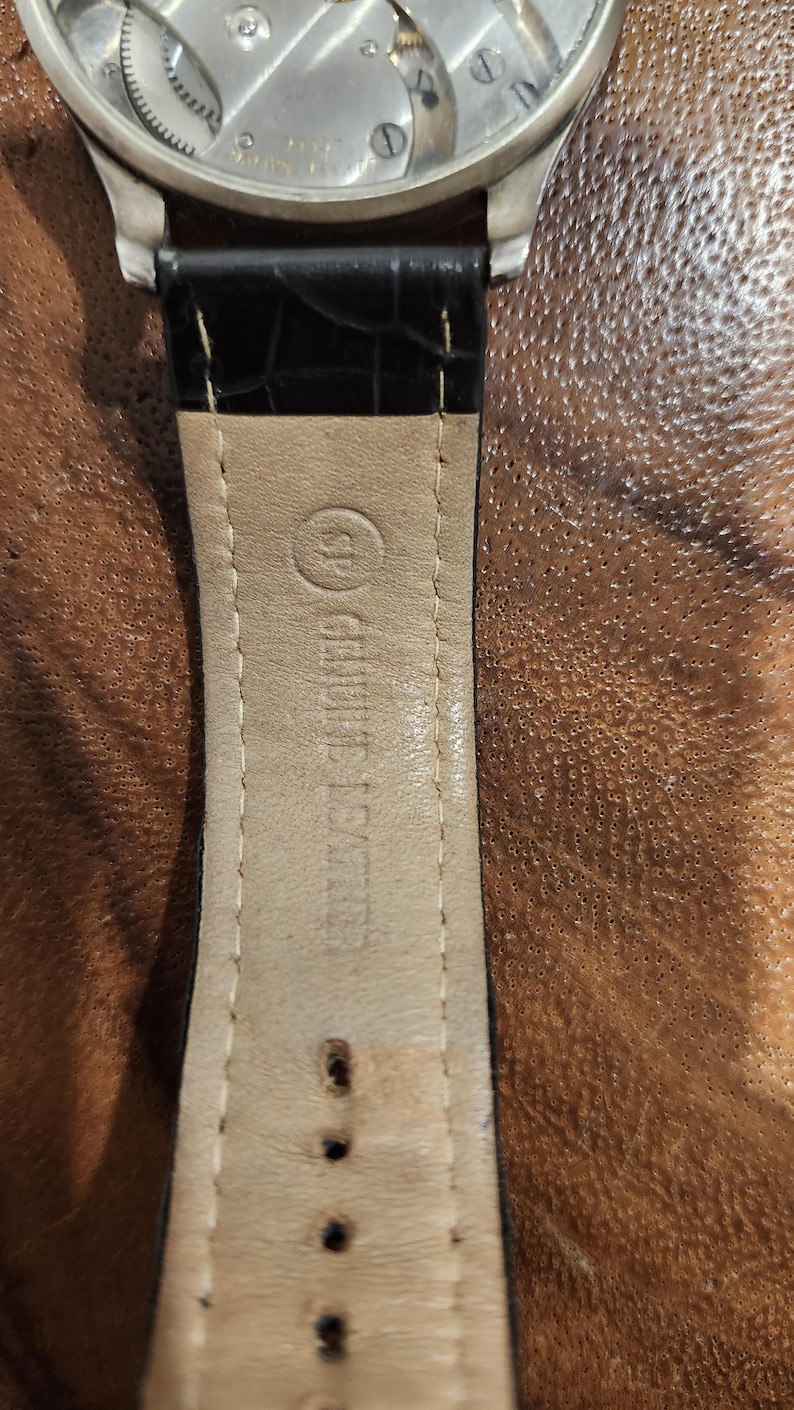 Puede incluir: Primer plano de una correa de reloj de cuero marr&oacute;n con costuras blancas. La correa tiene un forro de cuero blanco con el texto "Genuine Leather" impreso en &eacute;l.