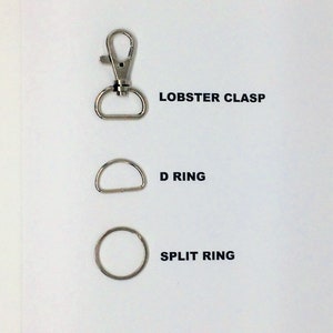Op de afbeelding: Drie metalen onderdelen: een karabijnhaak, een D-ring en een splitring. Deze worden vaak gebruikt om items aan tassen, sleutelhangers of andere accessoires te bevestigen.