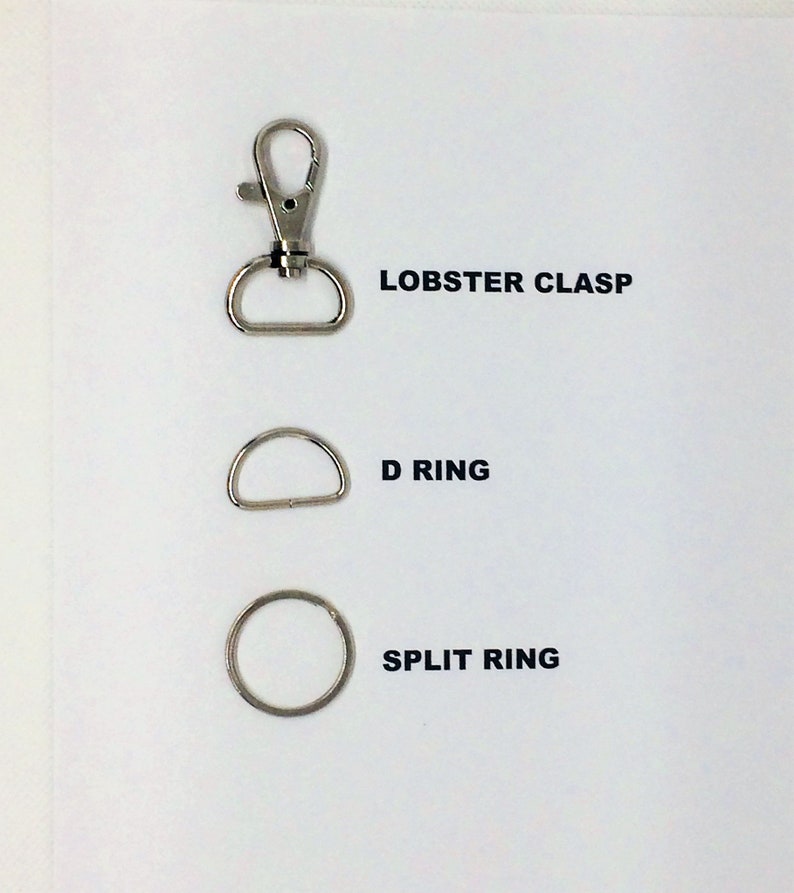 Op de afbeelding: Drie metalen onderdelen: een karabijnhaak, een D-ring en een splitring. Deze worden vaak gebruikt om items aan tassen, sleutelhangers of andere accessoires te bevestigen.