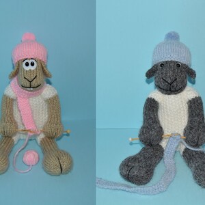 May include: Two knitted sheep dolls wearing hats and scarves, one with pink and one with blue accents, are holding knitting needles and yarn balls.