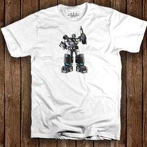 May include: White t-shirt featuring a detailed illustration of a black, gray, and blue robot holding a weapon. The robot has a complex design with mechanical details. The shirt has a crew neck and short sleeves. The brand logo is visible on the upper part of the shirt.