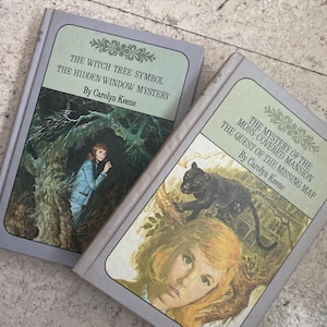 May include: Two vintage hardcover books with light blue covers. The book on the left is titled "The Witch Tree Symbol The Hidden Window Mystery" by Carolyn Keene. The book on the right is titled "The Mystery of the Moss-Covered Mansion The Quest of the Missing Map" by Carolyn Keene.