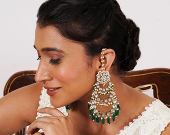 Può includere: Un paio di orecchini pendenti dorati e verdi con dettagli di perle bianche e pietre trasparenti. Gli orecchini presentano un design floreale e una catena che si collega all'orecchio.