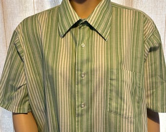 May include: A short-sleeved button-down shirt with vertical stripes in shades of green and off-white. The shirt has a classic collar, a chest pocket, and is displayed on a mannequin. The fabric appears to be a lightweight cotton or blend.
