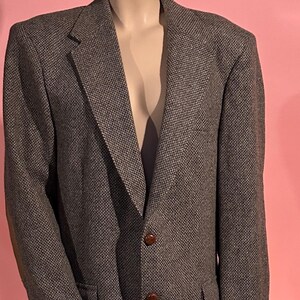 以下が含まれることがあります： クラシックなデザインの茶色のツイードブレザー。ノッチドラペル、2つのフロントポケット、茶色のボタンが特徴です。マネキンに着せたブレザーがピンク色の背景に展示されています。
