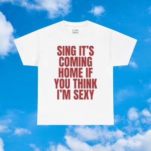 Op de afbeelding: Wit T-shirt met de tekst "SING IT'S COMING HOME IF YOU THINK I'M SEXY" in het rood. Het shirt heeft een ronde hals en korte mouwen. De merknaam "Little Weirdo" staat bovenaan.