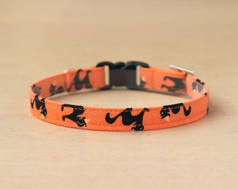May include: Orange cat collar with a black cat silhouette pattern. The collar has a black plastic buckle.