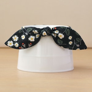 May include: A white ceramic cup with a black and white floral fabric bow tied around the top.