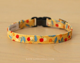 May include: A yellow cat collar with a red and white cherry print and blue leaves. The collar has a black plastic buckle.