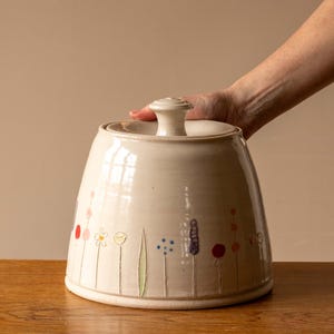 May include: White ceramic lidded jar with a floral design. The jar has a white knob on the lid and is decorated with pink, red, yellow, green, and purple flowers.