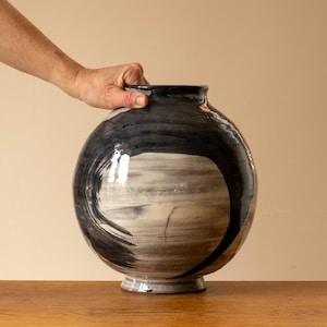 Könnte beinhalten: Eine große, runde Keramikvase mit einem abstrakten Design in Schwarz und Weiß. Die Vase hat einen breiten Boden und eine schmale Öffnung.