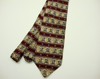 May include: A burgundy tie with a repeating pattern of gold and cream-colored floral and leaf motifs, interspersed with navy blue accents and small gold dots. The tie is displayed on a white background.