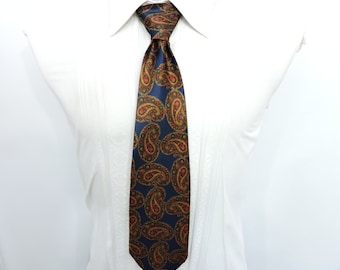 May include: A navy blue tie with a paisley pattern in shades of gold, red, and green. The tie is knotted and displayed against a white dress shirt, showcasing a classic formal accessory.