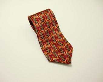 May include: A red tie with a repeating pattern of gold and black shapes, accented with small blue details. The tie is made of a shiny material and is displayed on a white surface.