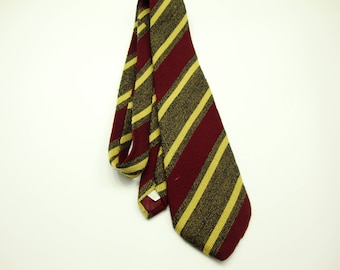 May include: A maroon and gold striped tie against a white background. The tie has alternating stripes of maroon and gold. The tie is made of a textured fabric and is hanging loosely.