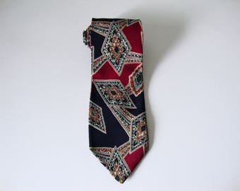 May include: A patterned necktie with a geometric design. The tie features navy blue, burgundy, and teal colours. The pattern includes diamond shapes with intricate details, creating a classic and stylish accessory.