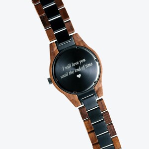 May include: A wooden and black metal wristwatch with a black face and an engraved message that reads "I will love you until the end of time" with a small heart symbol.
