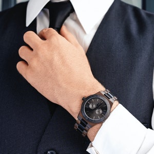 May include: A black and brown wooden wristwatch with a chronograph dial. The watch has a black leather band and a silver face with white markings.