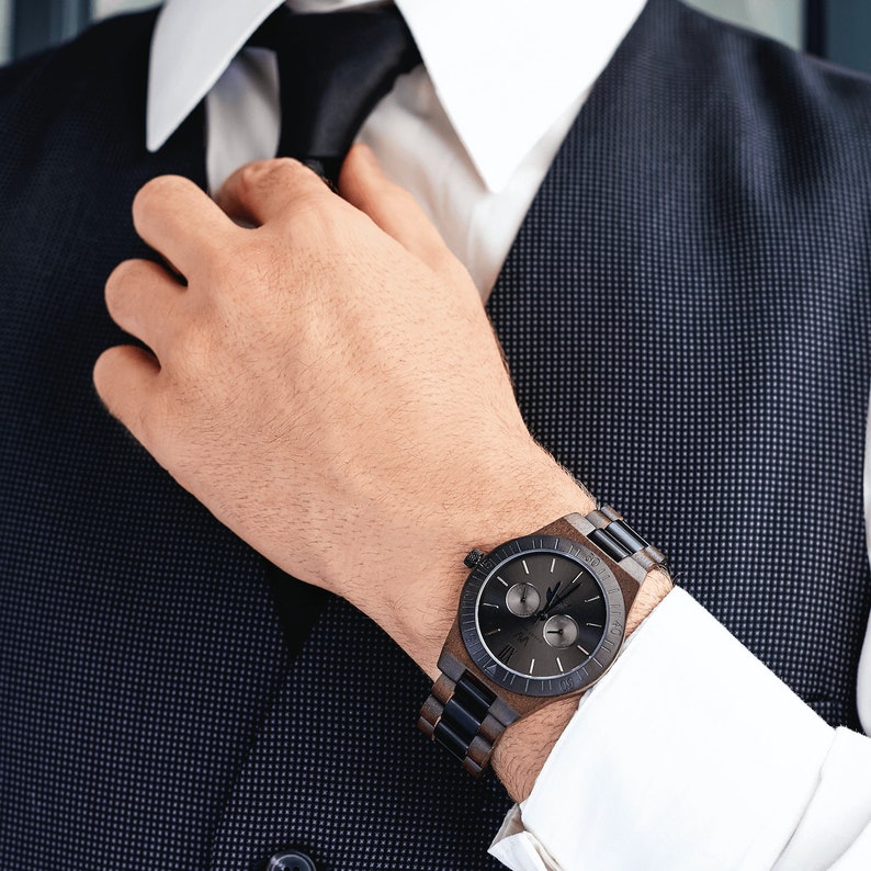 May include: A black and brown wooden wristwatch with a chronograph dial. The watch has a black leather band and a silver face with white markings.