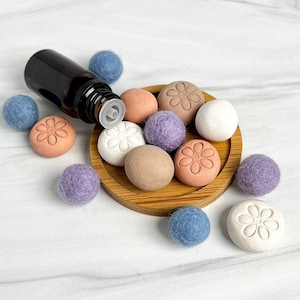 May include: A set of 10 diffuser balls in various colours, including purple, blue, brown, and white. The balls are made of felt and have a floral design. A small brown glass bottle with a dropper is also included.