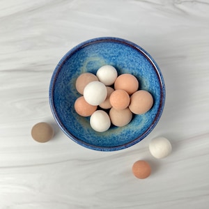 Könnte beinhalten: Eine blaue Keramikschüssel gefüllt mit verschiedenen kleinen, runden, beige und weißen Kugeln. Die Schüssel hat eine blaue und weiße gesprenkelte Glasur.