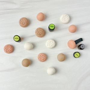 May include: A set of 12 aromatherapy diffusers, each with a flower design, in shades of brown and white. The diffusers are arranged on a white surface with three small bottles of essential oils labeled "Calm", "Relax", and "Patience".