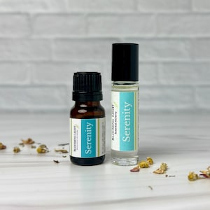 Puede incluir: Dos botellas de vidrio de aceite esencial con una etiqueta azul y blanca que dice "Serenity Blooming Light Botanical Alchemy".