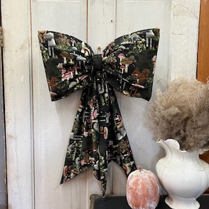 May include: A large black bow with a mushroom print. The bow is tied with a loop and has a long tail. The bow is made of fabric and has a shiny finish.