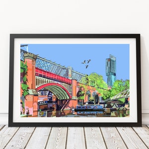 May include: A framed art print of a bridge over a canal, rendered in a stylized illustration. The bridge features red arches and a metal framework, with a modern skyscraper in the background. The sky is blue, and the print is in a black frame.