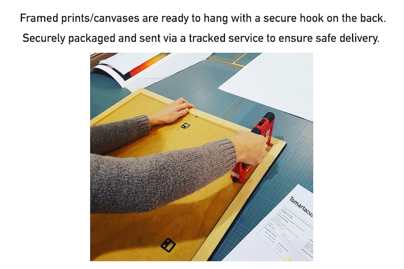 May include: A person using a red staple gun to attach the back of a framed print. The frame is light brown, and the back is a tan color. The text in the image says, "Framed prints/canvases are ready to hang with a secure hook on the back."