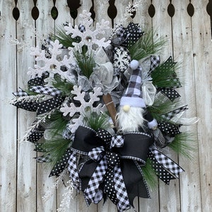 May include: A black and white Christmas wreath with a gnome holding skis, a black and white buffalo plaid bow, and white snowflakes.