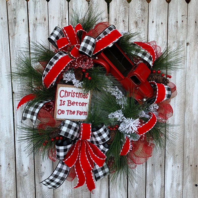 May include: A Christmas wreath with red and black buffalo check ribbon, a red truck, and a sign that says "Christmas is Better on the Farm".