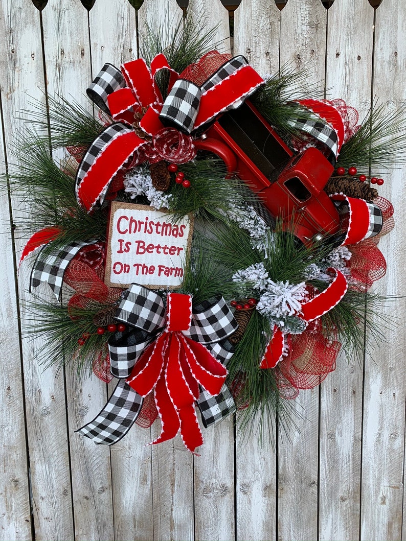 May include: A Christmas wreath with a red truck, red and black buffalo check ribbon, and a burlap sign that reads "Christmas Is Better On The Farm".
