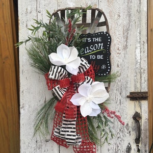May include: A Christmas wreath with a black and white striped ribbon, red mesh, white magnolia flowers, and a sign that says "It's the season to be jolly".
