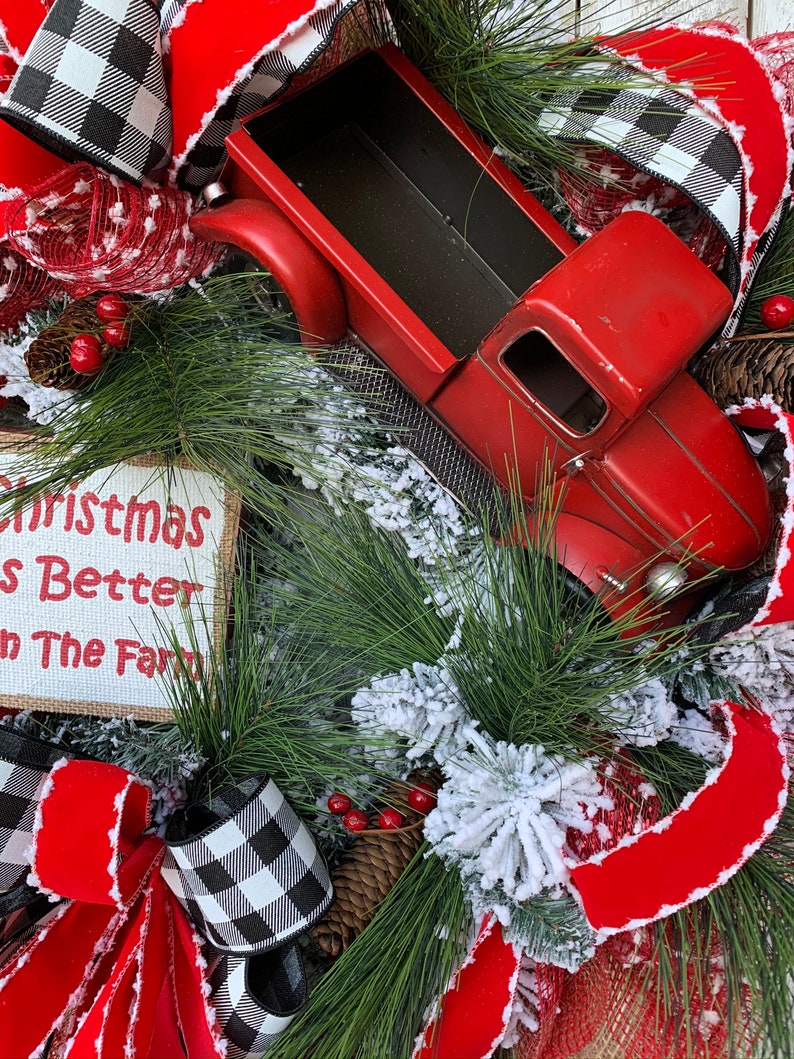 May include: A Christmas wreath with a red truck, red and black buffalo check ribbon, and a sign that reads "Christmas Is Better On The Farm".