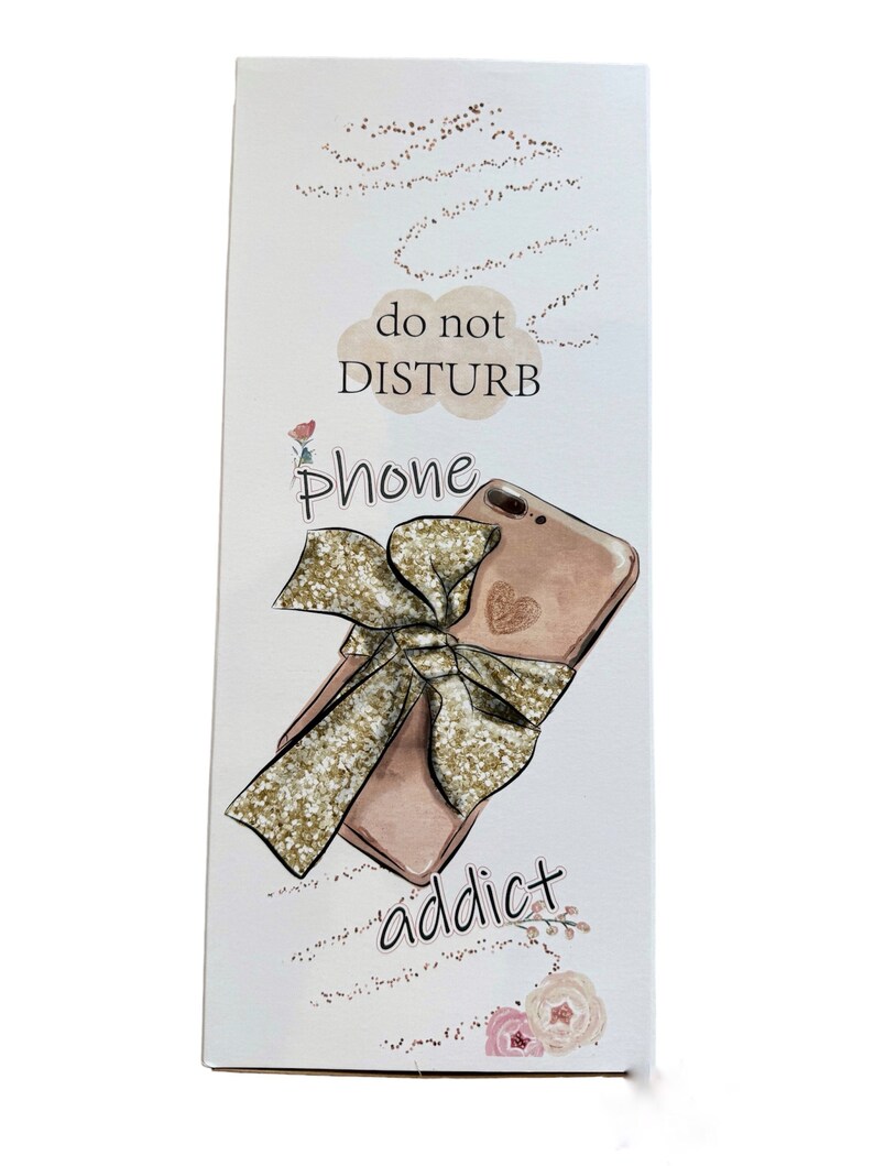 K&ouml;nnte beinhalten: Rechteckiges wei&szlig;es Schild mit einer Illustration eines ros&eacute;goldenen Telefons, einer goldglitzernden Schleife und den Worten "do not DISTURB" und "phone addict". Das Schild hat ein dekoratives Blumen- und Punktmuster.