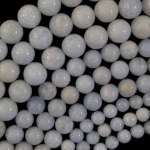 May include: A collection of smooth, light blue, round, polished stones. The stones are arranged in a curved pattern on a black background.