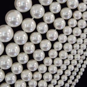 May include: A strand of white pearls arranged in a graduated pattern, featuring larger spheres at one end that gradually decrease in size toward the other end. The smooth, lustrous surface of each pearl reflects light, creating a bright appearance.