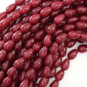May include: A strand of deep red gemstone beads in a teardrop shape. The beads are smooth and polished, with a glossy finish.