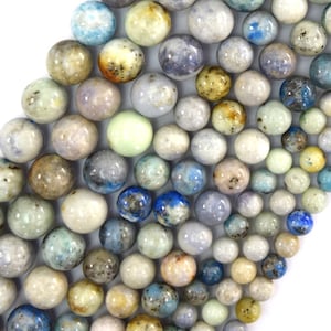 Puede incluir: Una hebra de cuentas redondas de piedras preciosas multicolores. Las cuentas son una mezcla de azul claro, blanco y marrón con motas de azul, marrón y blanco. Las cuentas tienen un diámetro aproximado de 8 mm.