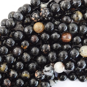 May include: A close-up of a pile of black and brown round beads. The beads are made of a natural stone with a speckled pattern.