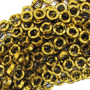 May include: A large pile of gold-colored metal beads with a wavy, textured surface. The beads are all the same size and shape, and they are arranged in a random pattern.